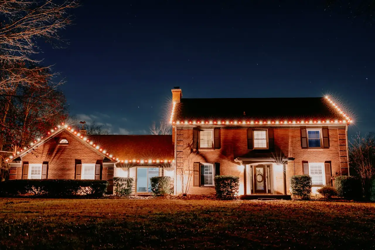 Christmas lights outlining the roofline of a two-story brick home at night